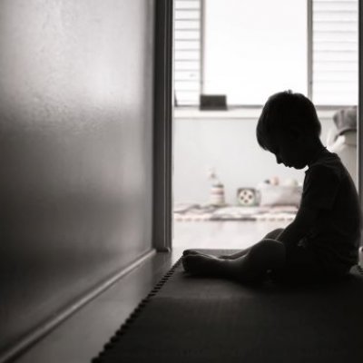 Child sitting in darkened hallway with head down. Adobe